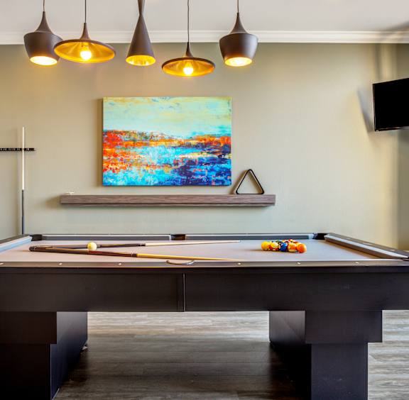 A pool table with a painting hanging above it.
