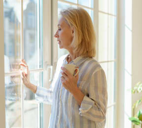 a woman looking out a window with a cup of coffee