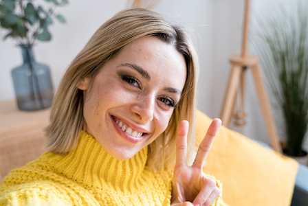 A woman in a yellow sweater is making a peace sign.