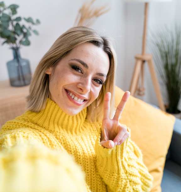 A woman in a yellow sweater is making a peace sign.