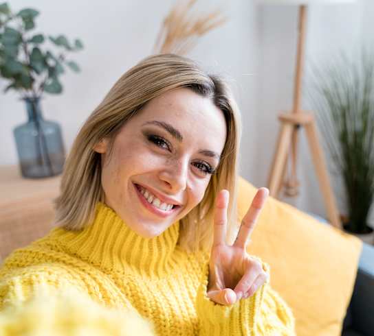 A woman in a yellow sweater is making a peace sign.