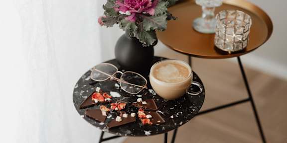 A table with a cup of coffee, a vase with flowers, and a chocolate dessert.