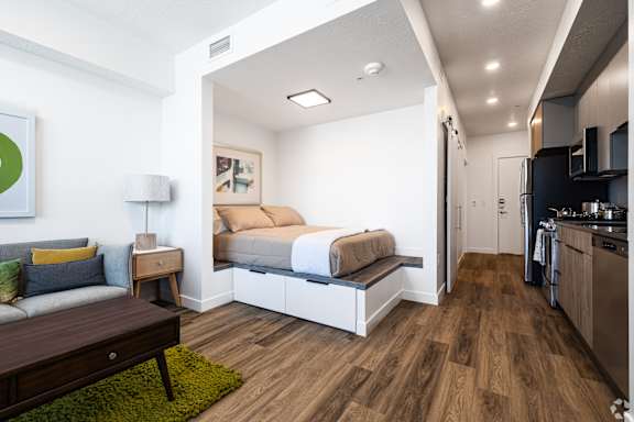 A modern kitchen with a breakfast bar and a bedroom with a built in bed.