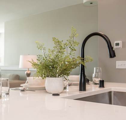 A kitchen counter with a sink, a vase with flowers, and some glasses.
