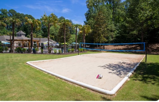 A sand volleyball court with a blue fence and a red object in the middle.