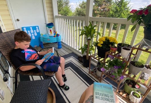 a young boy sitting in a chair reading a book on a porch