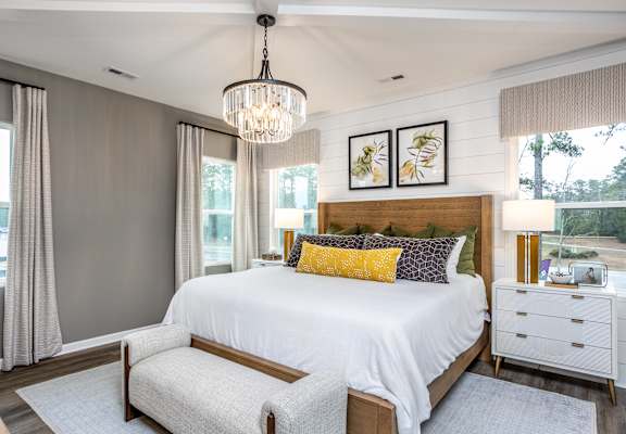 A bedroom with a large bed, a chandelier, and a window with curtains.