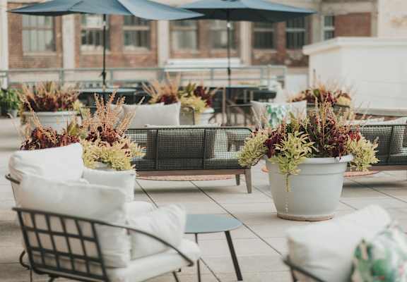A patio with white chairs and a large pot of plants.