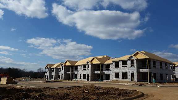 A row of houses under construction with a blue sky and clouds in the background.