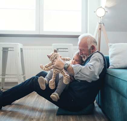 A man sitting on the ground, holding a baby and stuffed animal
