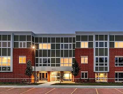 A modern building with a red brick facade and large windows is illuminated at dusk.
