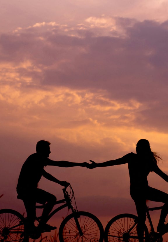 a man and woman holding hands while riding bikes at sunset
