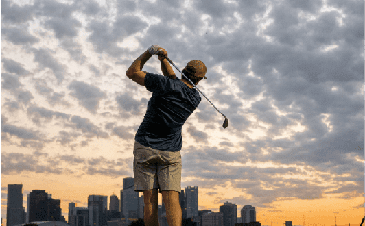 A man is playing golf in a field with a city skyline in the background.