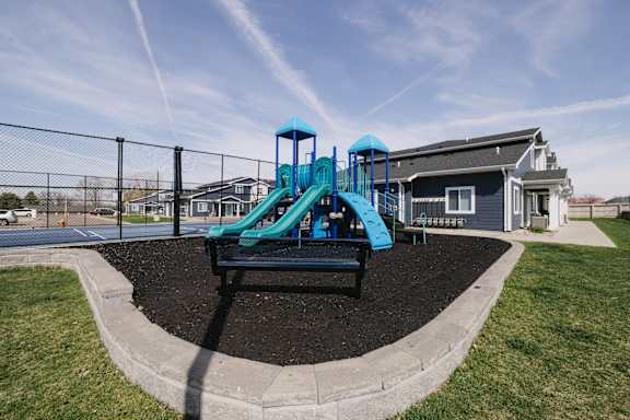 A playground with a blue slide and a black bench.