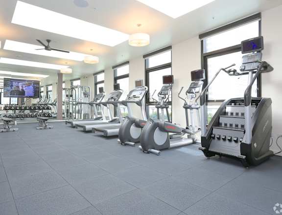 A spacious gym with a variety of equipment including treadmills, elliptical machines, and a television.