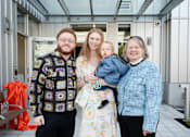Thumbnail 6 of 24 - A family of four stands in front of a building with the name "St Luke's" on it.