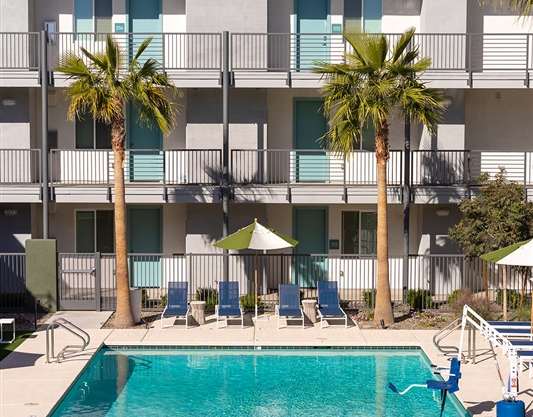 A pool surrounded by chairs and palm trees in front of a building.