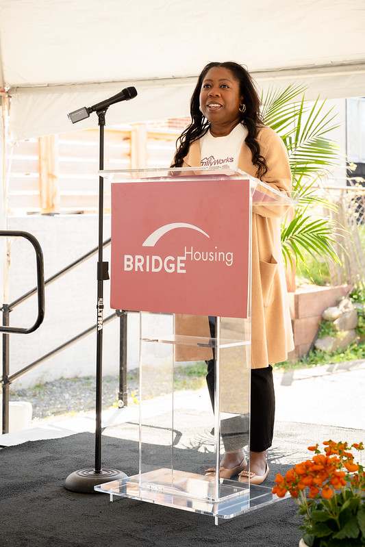 A woman is giving a speech at a podium with the words "BRIDGE Housing" on it.