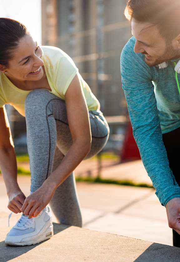 A man and a woman are tying their shoelaces outdoors.