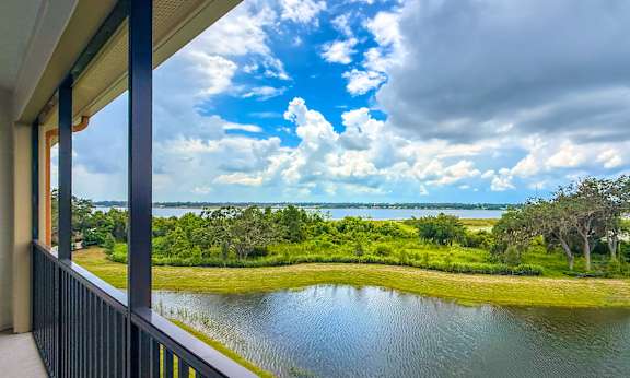 A balcony overlooks a body of water with a green landscape and trees in the distance under a blue sky with clouds.