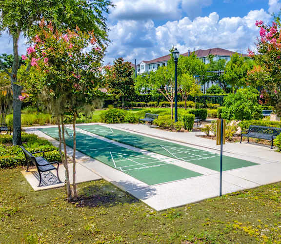 A green and white tennis court surrounded by trees and benches.