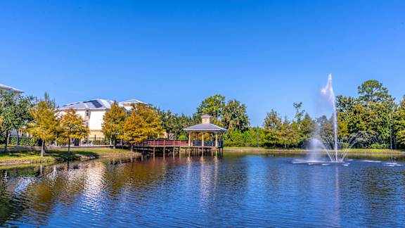 A serene lake with a fountain in the middle and a gazebo in the background.