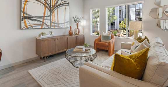 A living room with a large abstract painting on the wall, a white sofa, and a glass coffee table.