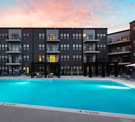 A large swimming pool in front of a building with a sunset in the background. at The Cunningham Apartments, West Des Moines