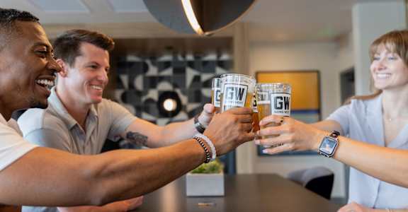 Three people toasting with glasses that have the letters "GW" on them.