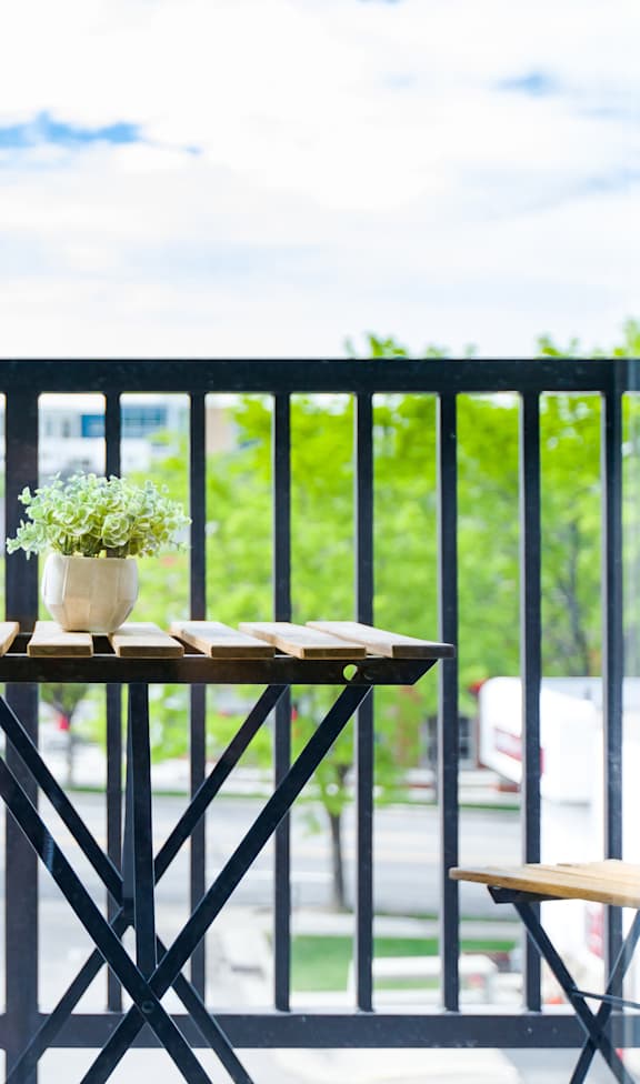 A table with a vase of flowers and a book on it is on a balcony  at Sugar House Apartments By Urbana, Salt Lake City, UT, 84105