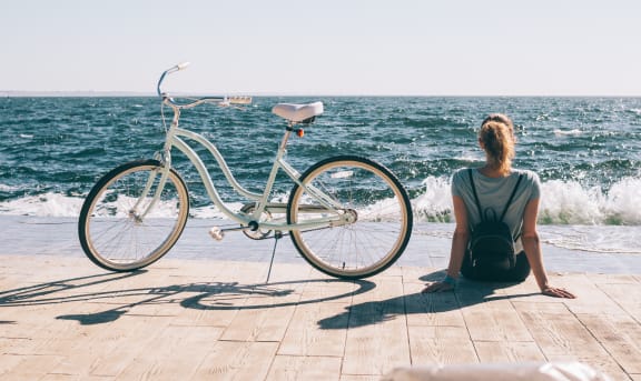 a woman sitting next to a bike on a dock by the ocean