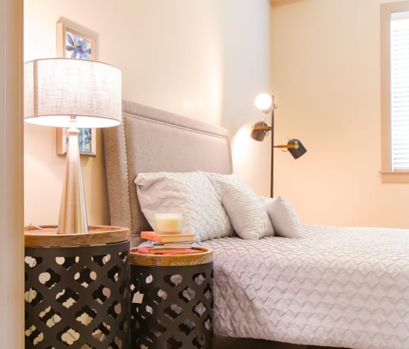 A bedroom with a bed, a lamp, and a table with a book on it at Sugar House Apartments By Urbana, Salt Lake City, UT, 84105
