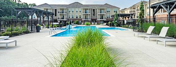 A pool area with a grassy divider in the foreground and a building in the background.