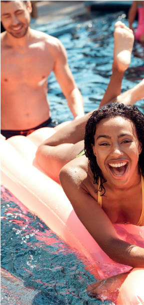 a smiling woman on a pool float in a swimming pool, with a man wading behind her