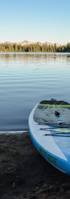 A blue and white paddleboard with the word "Norwegian" written on it is propped up against a body of water.