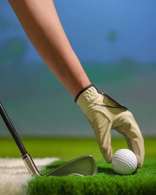 A person's hand in a glove is about to hit a golf ball with a golf club.