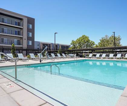 A large outdoor swimming pool with lounge chairs and a building in the background.