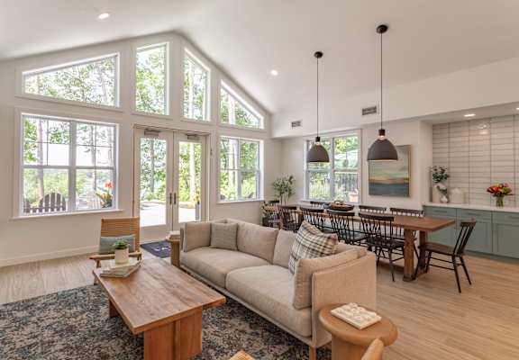 an open concept living room and dining room with large windows and a vaulted ceiling