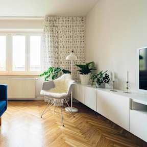 A blue sofa sits in a living room with a white chair and a television.
