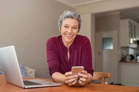 a woman sitting at a table with a laptop and cell phone