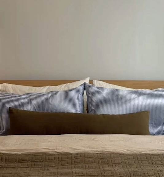 A bed with a white and blue striped pillow and a brown pillow.