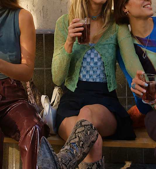 Three women sitting on a bench, one holding a drink.