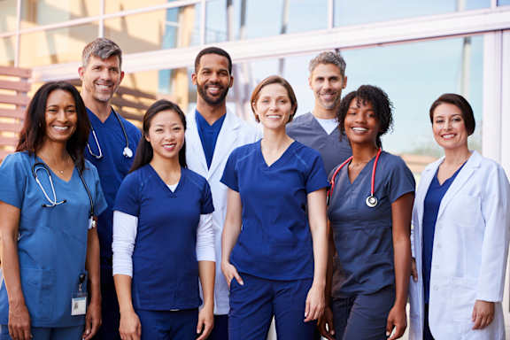 A group of medical professionals in blue scrubs and white coats stand together.