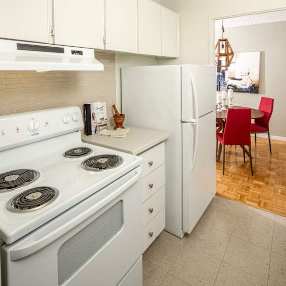 A kitchen with a white stove, white oven, white refrigerator, and a red chair.