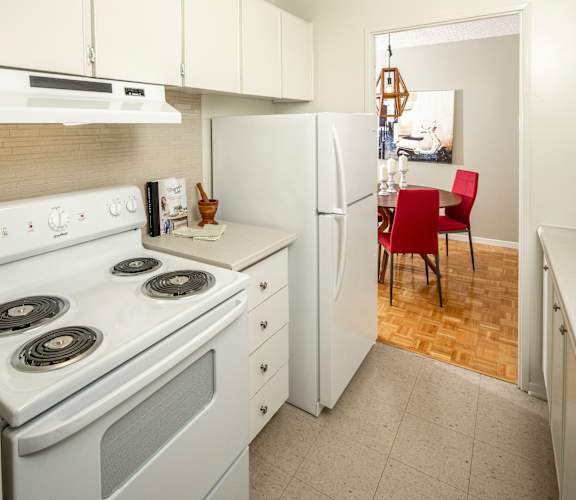 A kitchen with a white stove, white oven, white refrigerator, and a red chair.