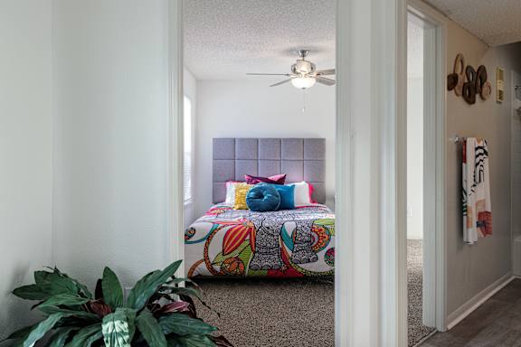A cozy bedroom in the model unit of Skyler Ridge Apartments, featuring a bed and ceiling fan.