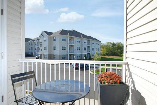 A balcony with a table and chairs overlooks apartment buildings.