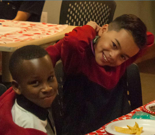 Two boys sitting at a table with food in front of them.