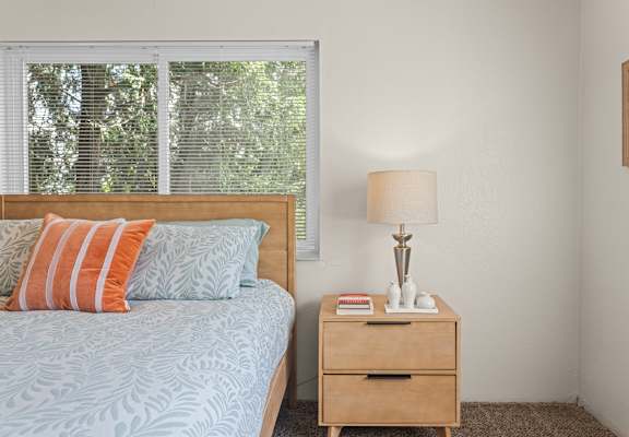 A bedroom with a bed, nightstand, and a window with blinds.