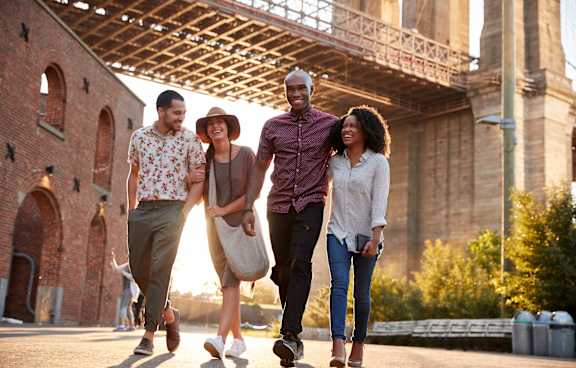 Four people walking together under a bridge.